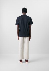 Schwarzes Baumwoll-T-Shirt mit kurzen Ärmeln, kombiniert mit beige-farbenen, locker sitzenden Hosen und bordeauxfarbenen Sneakers. Einfaches, minimalistisches Design.