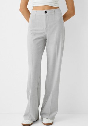 Pantalon large taille haute gris clair avec pli devant, bouton noir, porté avec des baskets blanches et un crop top blanc.
