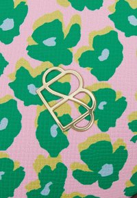 Růžová textilie se strukturovaným povrchem, zdobená zeleným a zlatým květinovým vzorem. Dominantní je zlatý emblém dvojitého "B".