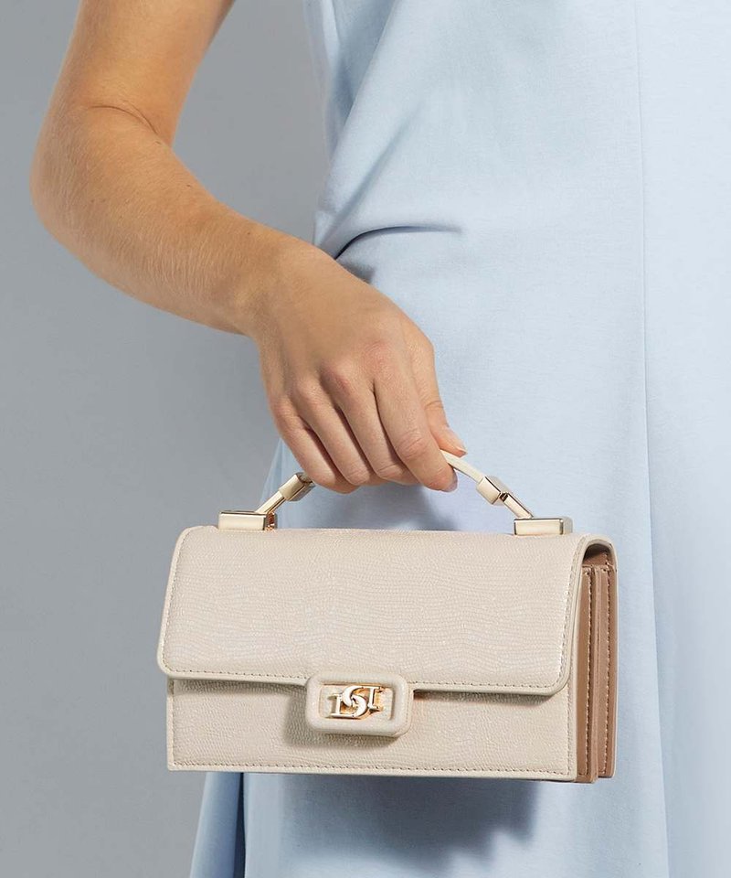 Main tenant un sac à main beige texturé avec une poignée dessus et un fermoir doré, sur une robe bleu clair et un fond gris.