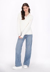 Hvid, langærmet pullover med lynlås halvkrave, parret med lyseblå, løst siddende jeans og hvide platform sneakers.