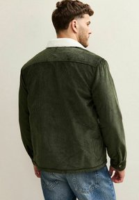 Chaqueta de pana verde con un cuello de borrego blanco, que presenta una textura acanalada y detalles de botones, mostrada desde la parte posterior contra un fondo claro.