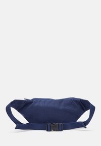 Marinblå tygmidjeväska med texturerad yta, justerbar rem och plastspänne, med en rundad design och minimalistisk stil.