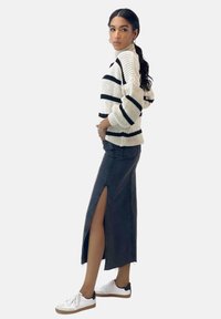 Tjockstickad tröja i creamfärg med svarta ränder, parat med en svart denimkjol med en sidoklyvning och vita sneakers med svarta detaljer.