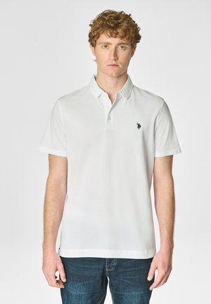 Polo bianca con colletto classico, maniche corte e un piccolo logo di un cavallo navy sul lato sinistro del petto, abbinata a jeans in denim blu.