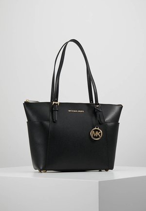 Zwarte leren totebag van Michael Kors met dubbele schouderbanden, gouden logo-hangertje en ritssluiting bovenop, gepresenteerd op een wit voetstuk.