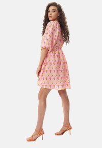 Short pink dress with floral patterns, puff sleeves, cinched waist, and flared skirt. Paired with orange strappy heels. Textured fabric.