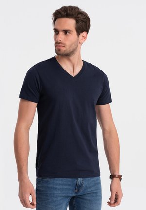 T-shirt en coton bleu marine avec un col en V, des manches courtes et une coupe slim. Présente une petite étiquette de marque sur le côté gauche près de l'ourlet.