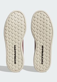 Suola di scarpa con fondo in gomma beige caratterizzato da un motivo testurizzato circolare e un logo centrale in nero. Bordo superiore liscio in un colore tenue.