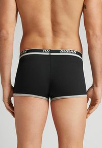 Boxers negros con textura acanalada, con una amplia cinturilla elástica con detalles plateados y una marca en la parte trasera.