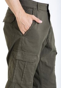Pantalons cargo vert olive en coton, dotés de plusieurs poches et d'une coupe décontractée. Le tissu a une apparence douce et texturée.