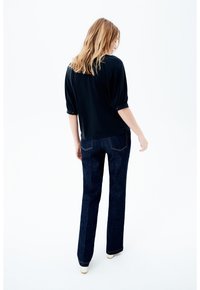 Suéter negro con mangas remangadas combinado con jeans acampanados de un azul oscuro. Detalles de costura sutil y una textura de tela suave. Fondo liso.