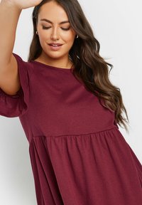 Viininpunainen lyhythihainen mekko, jossa on pyöreä pääntie, flare-hihat ja rypytetty vyötärö, valmistettu pehmeästä ja kevyestä kankaasta.