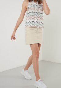 Koszula bez rękawów, zapinana na guziki, w kwiatowy wzór w pastelowych kolorach, zestawiona z beżową mini spódnicą i białymi, masywnymi sneakersami.