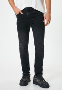 Jeans negros ajustados de corte recto con una textura suave, detalles de desvanecimiento sutil y un diseño clásico de cinco bolsillos, combinados con zapatillas negras.