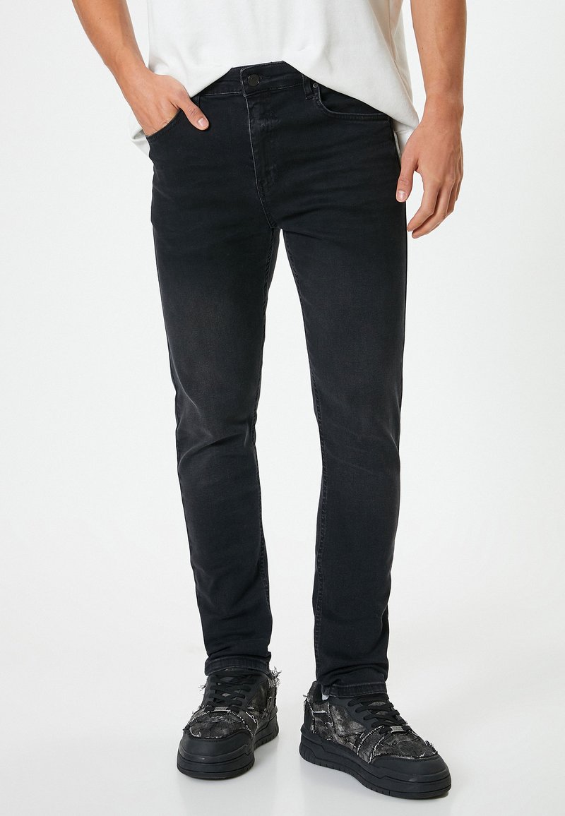Jeans negros ajustados de corte recto con una textura suave, detalles de desvanecimiento sutil y un diseño clásico de cinco bolsillos, combinados con zapatillas negras.