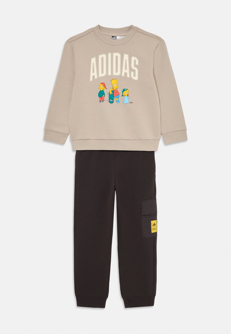 Beige sweatshirt with "ADIDAS" text and cartoon characters. Black pants with cargo pocket and yellow logo label. Soft fabric, relaxed fit.