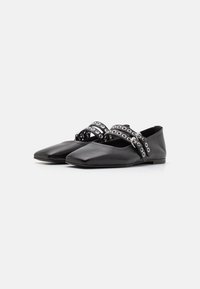 Chaussures plates en cuir noir avec un bout pointu, dotées d'une large bride avec des découpes circulaires argentées et d'une semelle basse et flexible.