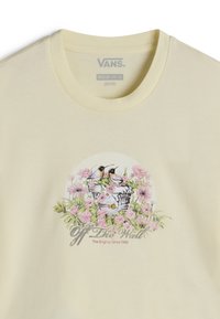 Light yellow t-shirt features a floral graphic with two birds and the text “Off The Wall” in the center. Soft cotton material, short sleeves.