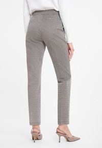 Pantalons ajustés en tissu à motifs présentant un design géométrique dans des tons neutres. Silhouette cintrée avec une taille mi-haute.