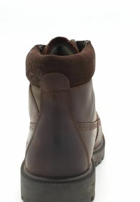 Stivaletto in pelle marrone e suede con collo imbottito e suola robusta, mostrato da dietro su uno sfondo bianco.