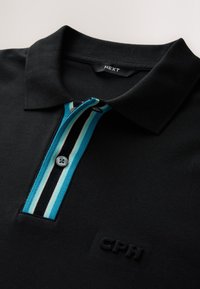 Polo negro con tapeta de botones con rayas azules, blancas y negras, cuello, y sutil logo CPH en relieve en el pecho.