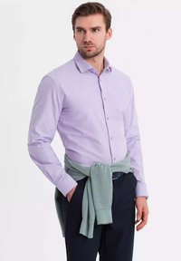 Camisa de manga larga de color púrpura claro con un diseño de botones, combinada con un suéter de punto verde menta atado en la cintura, usado con pantalones oscuros.
