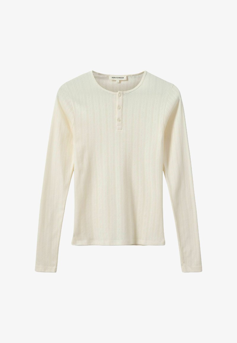 Hosszú ujjú krémszínű felső bordázott anyagból, texturált levélmintával. Kerek nyakkivágással és három gombbal rendelkezik elöl.