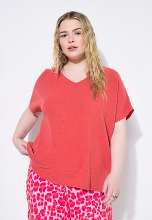 Korall V-hals t-shirt med løstsiddende pasform og tekstureret stof, parret med lyserøde bukser med et dristigt dyremønster.