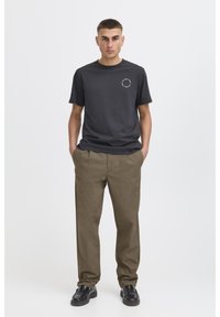 Dark gray cotton t-shirt with short sleeves, featuring a small graphic on the chest, paired with light brown loose-fit trousers and black shoes.