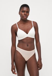 White, smooth fabric bra with thin straps and a V-neck design; paired with beige, semi-sheer hipster briefs featuring a soft waistband.