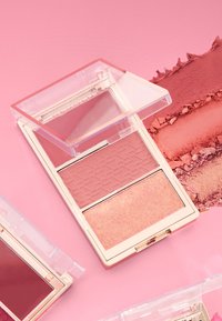 Kompakt rødmepalett med to nyanser: en matt lys rosa med mønstret overflate og en shimmery fersken. Gjennomsiktig etui med gullfargede detaljer.