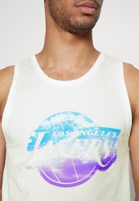 Biała bezrękawnikowa koszulka z multikolorową grafiką koszykówki oraz napisem "Los Angeles Lakers" w pogrubionych literach, z przejściem kolorów od niebieskiego do fioletowego.