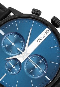 Montre chronographe noire avec un cadran texturé bleu, trois sous-cadrans, des accents argentés et un bracelet en cuir noir élégant. Logo de la marque : OOZOO.