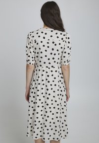 Vestido blanco con lunares negros, hasta la rodilla, con mangas abullonadas y escote redondo. Tejido suave con un corte holgado.