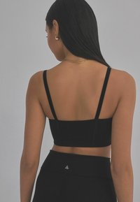 Sort cropped bra-top med tynde stropper, glat tekstur og minimalistisk design. Har en logoaccent nær kanten.