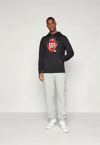 Sweatshirt preto com capuz e um gráfico de futebol na frente, combinado com calças cargo cinzas e ténis brancos. Conjunto simples e casual.