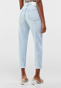 Lichtblauwe high-waist jeans met een ontspannen pasvorm, opgerolde boorden en twee achterzakken. Gladde denimtextuur. Gecombineerd met sandalen met transparante hakken.