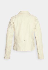 Giacca in pelle color crema caratterizzata da un design strutturato, collo a scollo a V, dettagli trapuntati sulle spalle e polsini con cerniera.