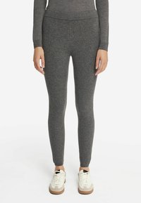 Leggings grigi in tessuto elasticizzato con una superficie liscia e un design aderente, abbinati a sneakers bianche con un accento beige e una suola testurizzata.