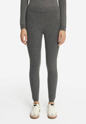 Leggings grigi in tessuto elasticizzato con una superficie liscia e un design aderente, abbinati a sneakers bianche con un accento beige e una suola testurizzata.