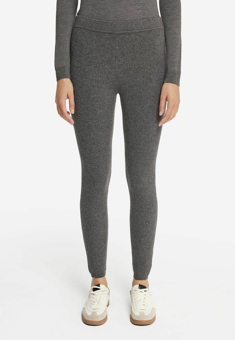 Leggings grigi in tessuto elasticizzato con una superficie liscia e un design aderente, abbinati a sneakers bianche con un accento beige e una suola testurizzata.