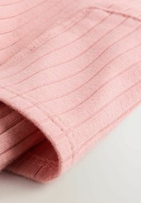 Vaaleanpunainen strukturoitu kangas, jossa on pystysuora uritus. Lähikuva, jossa näkyy pehmeä materiaali ja helmakuviot. Kevyt kiilto näkyvissä.