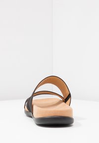 Une sandale noire de type slide avec une semelle intérieure rembourrée couleur tan et une semelle noire basse vue du talon sur fond blanc.