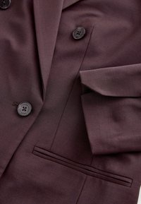 Blazer bordeaux à double boutonnage, avec de grands boutons noirs et un détail de poche élégant au fini texturé subtil.