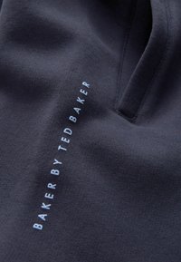 Jūras flotes kokvilnas audums ar maigu tekstūru, uz kura ir gaismas zilā krāsā izšūts "BAKER BY TED BAKER" logo. V veida dekoltē ar izsmalcinātu griezumu.