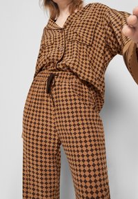Brun mönstrat loungedress med v-ringning, två bröstfickor och elastisk midja med dragsko, tillverkad av mjukt tyg.