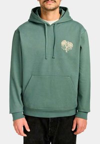 Sudadera con capucha en algodón verde apagado, que presenta un diseño floral en forma de corazón de color crema en el pecho y un bolsillo canguro en la parte frontal.