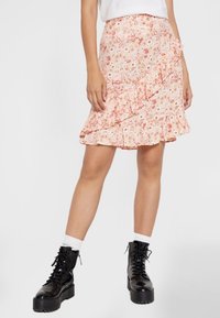 Bloemrijke, gerimpelde rok in pastelroze met kleine bloemen. Lichtgewicht stof, knielang, gecombineerd met zwarte veterschoenen en witte sokken.