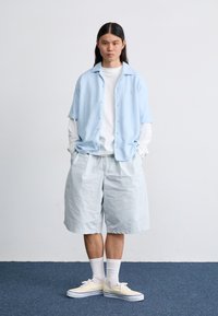Light blue short-sleeve button-up shirt, white long-sleeve shirt underneath, light blue shorts, white socks, and yellow sneakers.